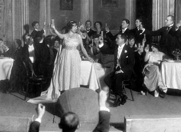 Scena i6 G. Verdi operos „Traviata“, 1920 m. Valstybės teatras Kaune. Centre stovi A. Galaunienė (Violeta), sėdi – K. Petrauskas (Alfredas)